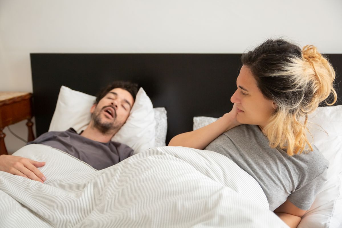 Couple in bed while the man snores and the woman lies awake